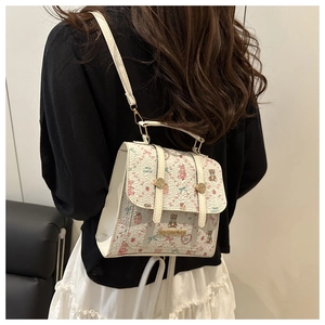 Close-up of white mini backpack with bear and bow prints and gold metal logo plaque