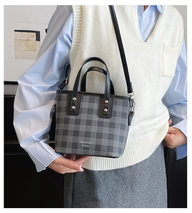 Detail of grey plaid bucket bag featuring black handles and adjustable shoulder strap
