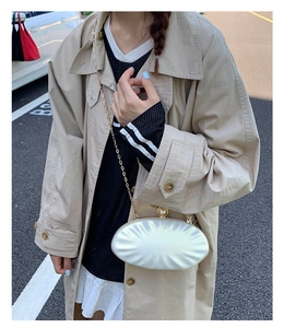 White shell-shaped evening bag with pearl clasp and gold chain strap worn by model