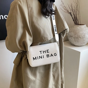 White mini crossbody bag with wide logo strap and litchi grain texture on trench coat model