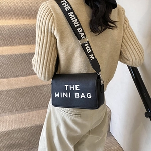 Street style black mini crossbody bag with wide letter strap worn by a female model