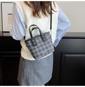 Plaid crossbody bucket bag with black top handles shown on model in a minimalist setting