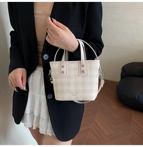 Detail of checkered bucket bag with dual handles, beige pattern and metal rivets