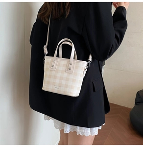 Side view of cream checkered bucket bag with dual handles and detachable shoulder strap