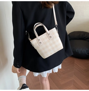 Detail of cream plaid bucket bag with adjustable strap and metal hardware on model