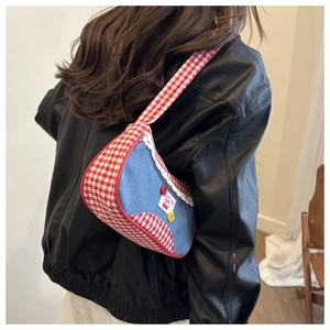 Detail of blue denim shoulder bag with red plaid trim and delicate lace edges