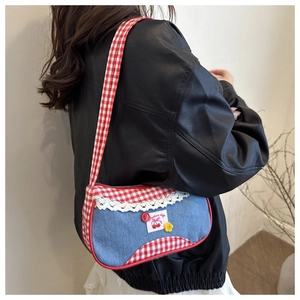 Close-up of denim shoulder bag with red plaid trim and lace detailing on a female model