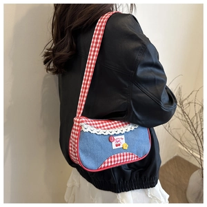 Close-up of a blue denim shoulder bag with red gingham trim and sweet cherry patches