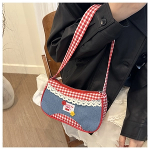 Detail of red checkered shoulder bag with lace edges and denim patch on a model
