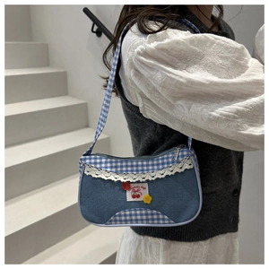 Close-up of denim and plaid shoulder bag with lace edges and flower pendants