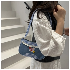 Detail of blue denim shoulder bag with white lace trim and cherry pattern patch