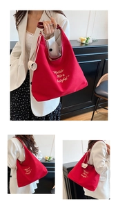 Detail of red canvas tote bag featuring white embroidery and a round charm detail