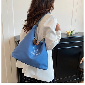 Detail of blue canvas tote bag with letter print and brown leather charm on shoulder strap
