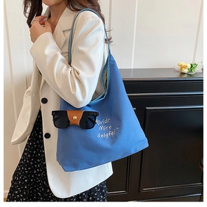 Blue canvas tote bag detail featuring white embroidered text and a leather sunglass holder clip