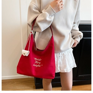 Detail of red canvas tote bag featuring white script lettering and a small white pouch