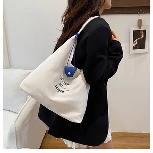 Detail of white canvas tote bag with black embroidery and blue decorative pendant charm