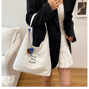 Detailed shot of white canvas tote bag with artistic letter print and blue charm pendant