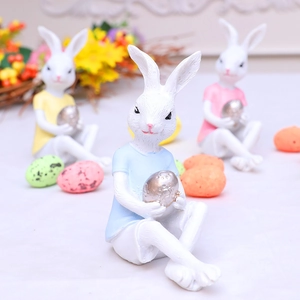 Three Easter bunny resin figurines holding eggs in pink, blue, and yellow outfits