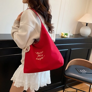 Red fabric tote bag with white letter embroidery and adjustable straps in a modern setting
