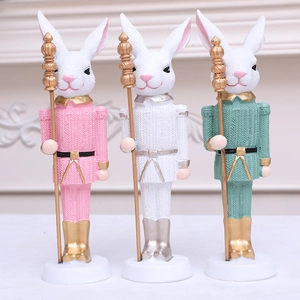 Three Easter bunny nutcracker figurines in pink, white, and teal holding golden scepters