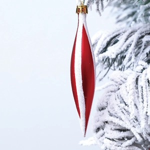 Macro detail of red spindle-shaped Christmas ornaments with white glitter stripes on snowy pine