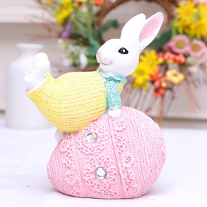 Figura de conejo de Pascua de resina con suéter amarillo sentado en un huevo decorativo