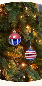 Close-up of star and stripe Christmas balls hanging on a pine tree with warm light bokeh