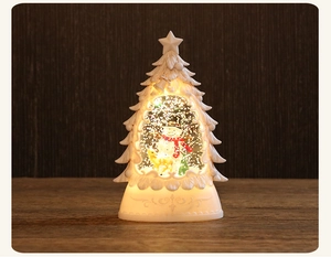 Close-up of a lit white Christmas tree snow globe with a snowman and warm glowing light