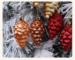Detailansicht von roten und goldenen Zapfenanhängern an verschneiten Weihnachtsbaumzweigen