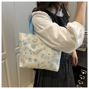Close-up of white tote bag with blue graffiti prints and matching woven shoulder straps