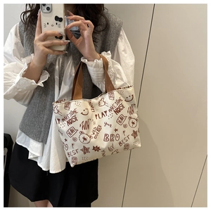 Detail of canvas tote bag with graffiti prints and brown strap handles on female model