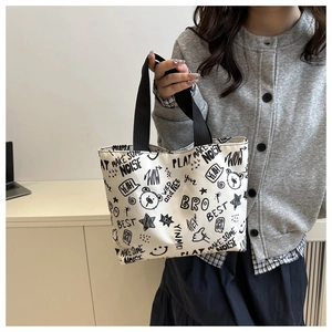 Detail of white graffiti tote bag with black cartoon patterns and woven handles