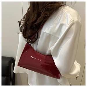 Model wearing a wine red patent leather baguette bag over a white silk blouse