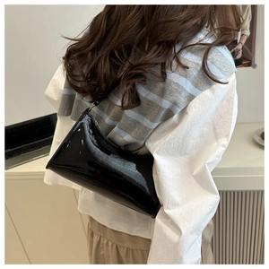Close-up of black patent leather underarm bag with glossy finish on a shoulder