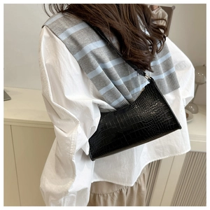 Detail of a black crocodile-pattern underarm bag on model with gold-tone metal hardware