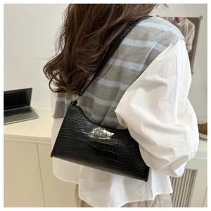 Detail of black crocodile texture baguette bag with golden buckle and leather strap