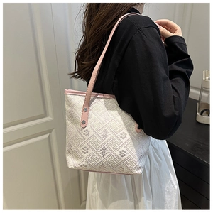 Dettaglio della trama ricamata e tracolla rosa della borsa a secchiello beige sul modello