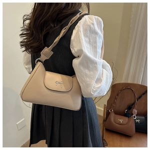 Close-up of cream faux leather baguette bag with silver bow hardware and woven strap