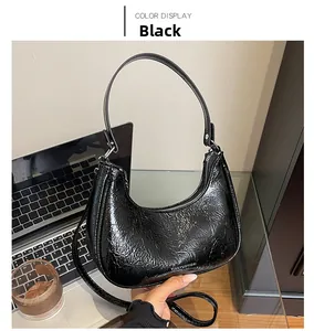 Détail du sac hobo croissant noir brillant avec texture froissée sur un bureau
