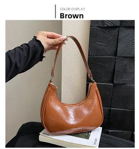 Détail d'un sac marron montrant le cuir plissé brillant et le logo de la marque