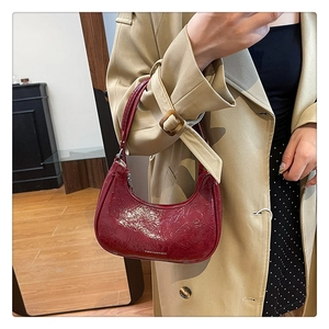 Détail du sac demi-lune bordeaux en cuir verni brillant sur un trench-coat de couleur kaki