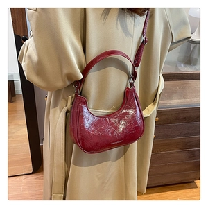 Sac croissant bordeaux chic en cuir verni plissé porté par un mannequin en manteau beige