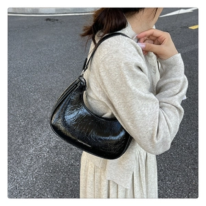 Détail d'un sac demi-lune noir en cuir verni brillant porté à l'épaule pour un look chic
