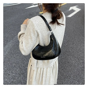 Vue arrière d'un sac demi-lune noir en cuir brillant plissé porté à l'épaule