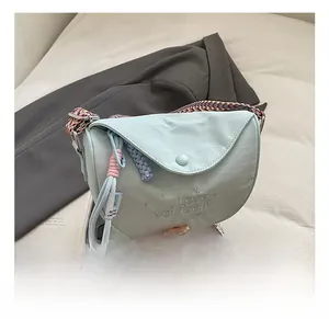Detail of light blue textured shoulder bag with colorful braided strap and embroidery
