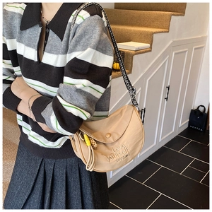 Beige crescent crossbody bag with embossed lettering and yellow pendant shown on model