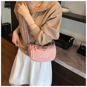 Pink crescent crossbody bag with colorful woven strap and embroidered text detail