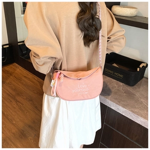 Pink crescent crossbody bag with white embroidery and woven shoulder strap on model