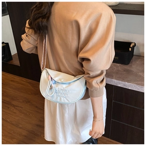 Detail of light blue crescent shoulder bag with embroidery and woven strap worn by model