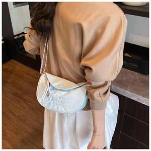 Detail of light blue crescent shoulder bag with embroidery and woven strap worn by model